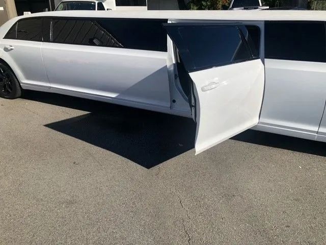 White stretch limousine with a door open on a paved street.