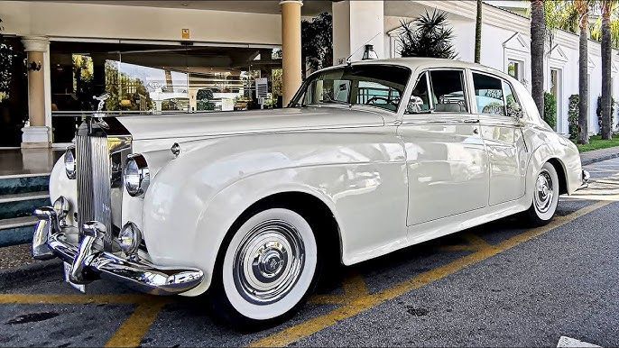 White vintage Rolls-Royce sedan parked in front of a building with columns and palm trees.