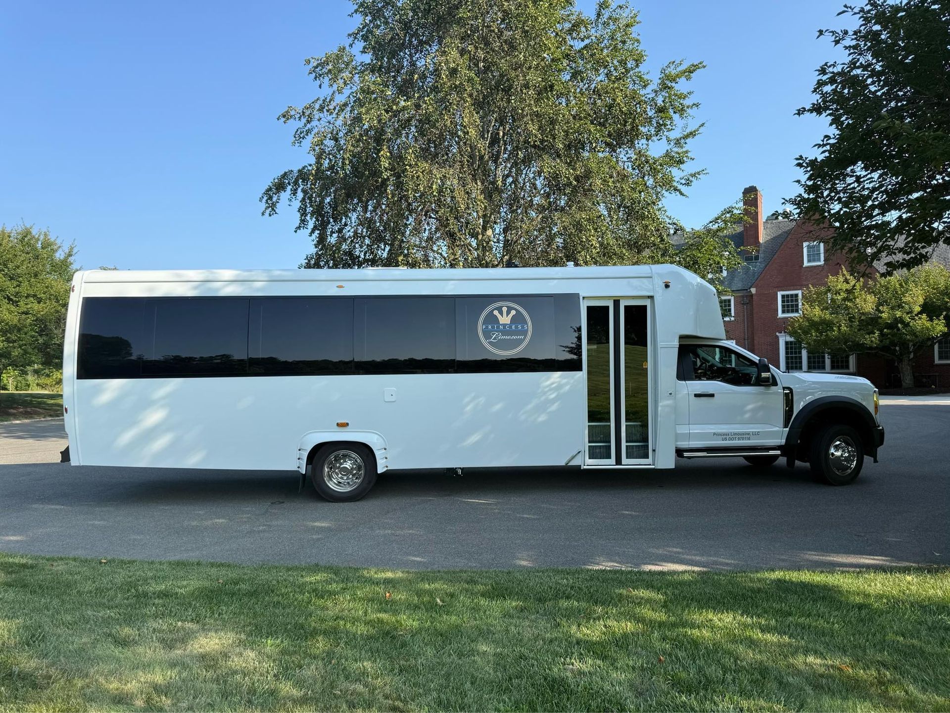 White passenger bus parked on a driveway with trees and a building in the background.