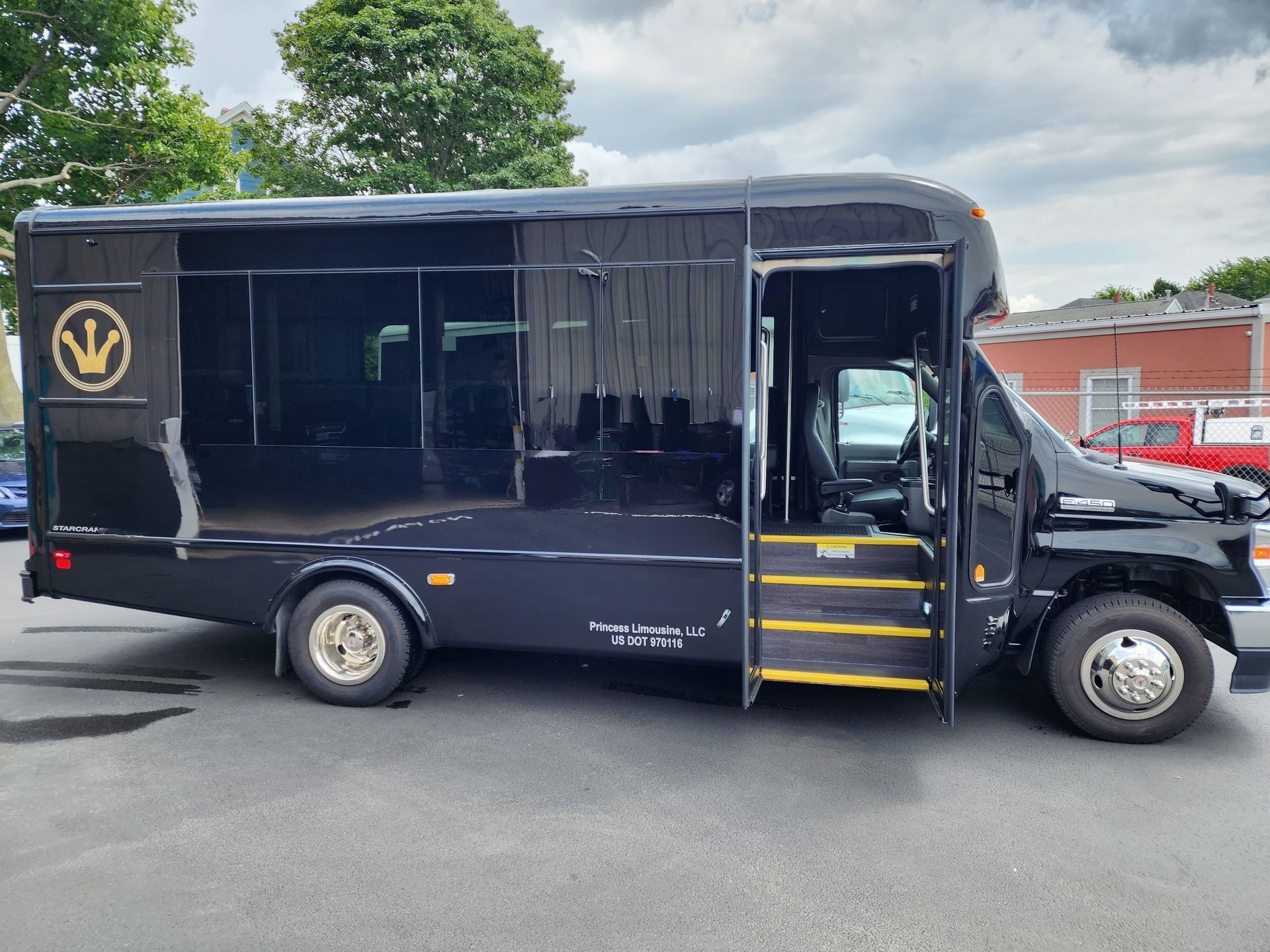 Black bus with open door; gold logo on side; parked on asphalt.