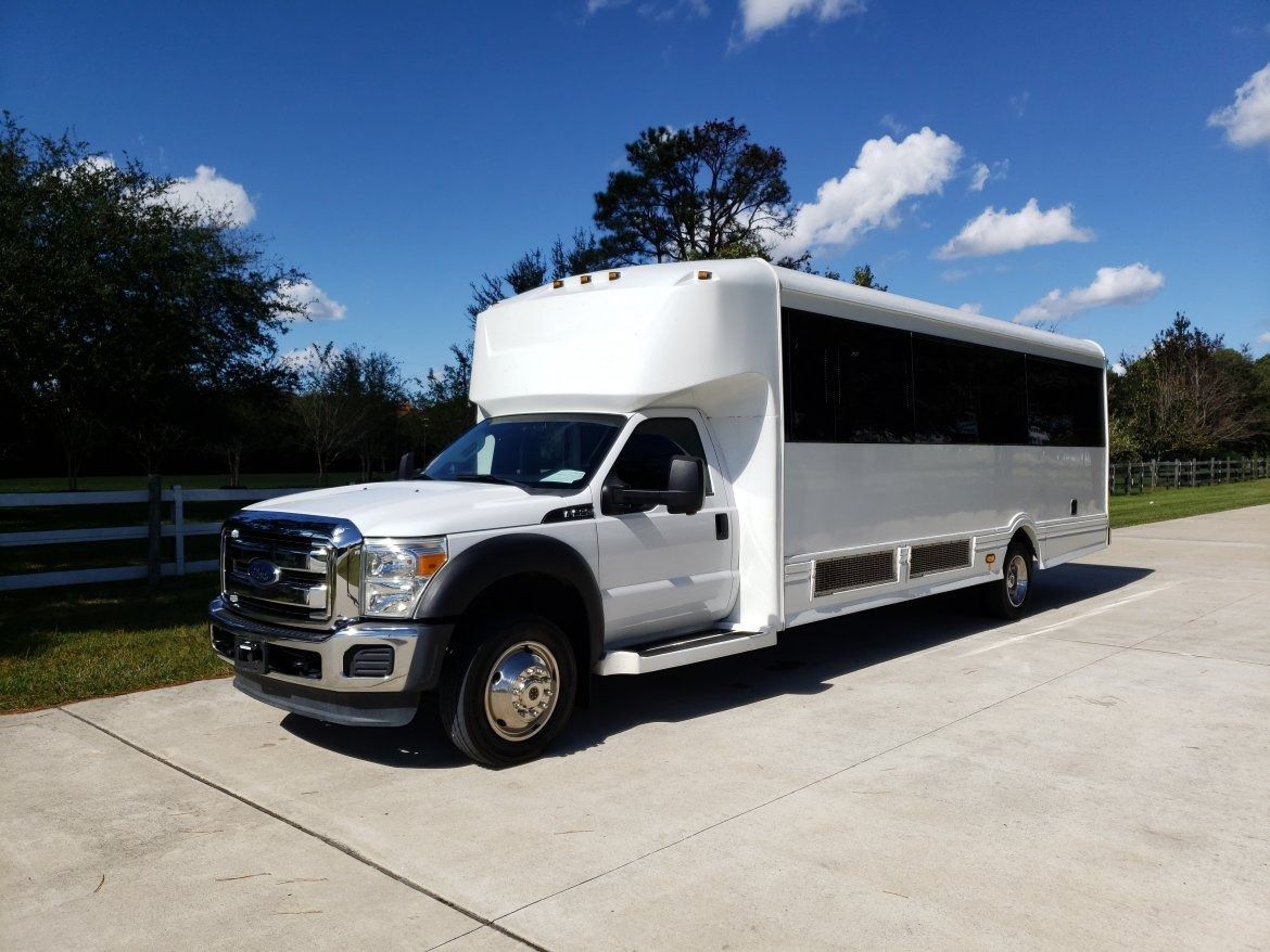 White party bus parked on a paved road on a sunny day with blue sky and clouds.