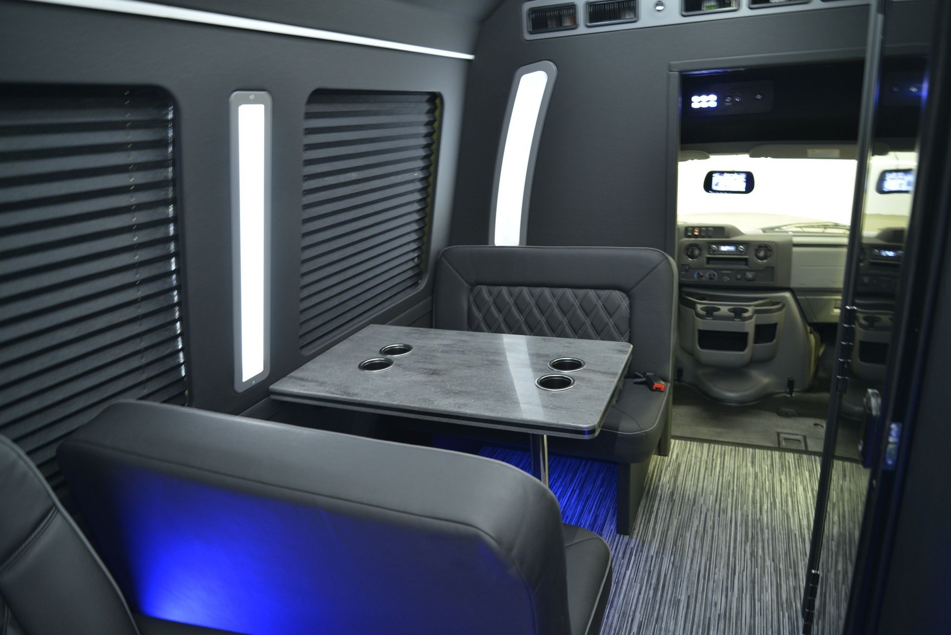 Interior of a black luxury van with seating, a table, and blue under-seat lighting.