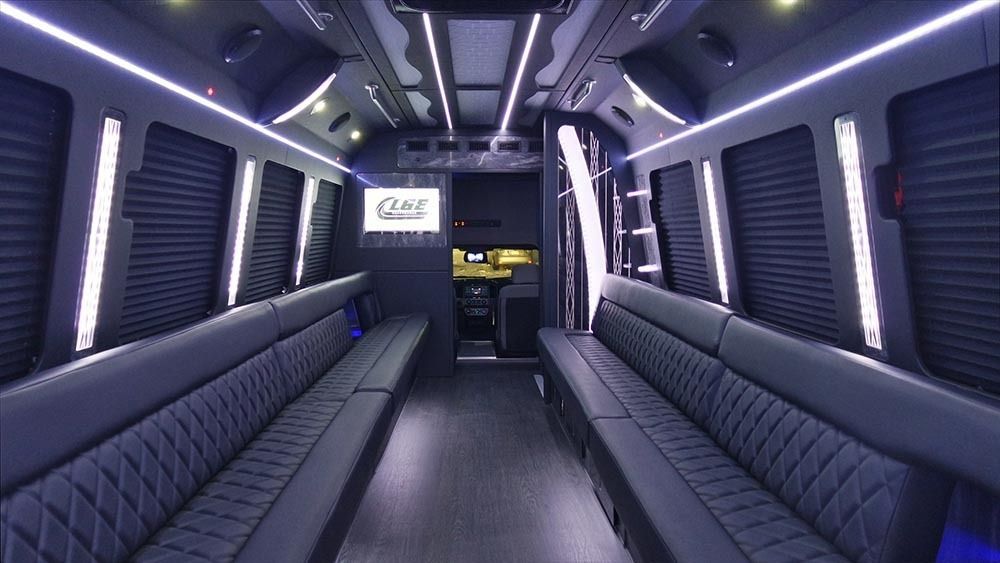 Interior of a black luxury van with leather seating, ambient lighting, and a TV.