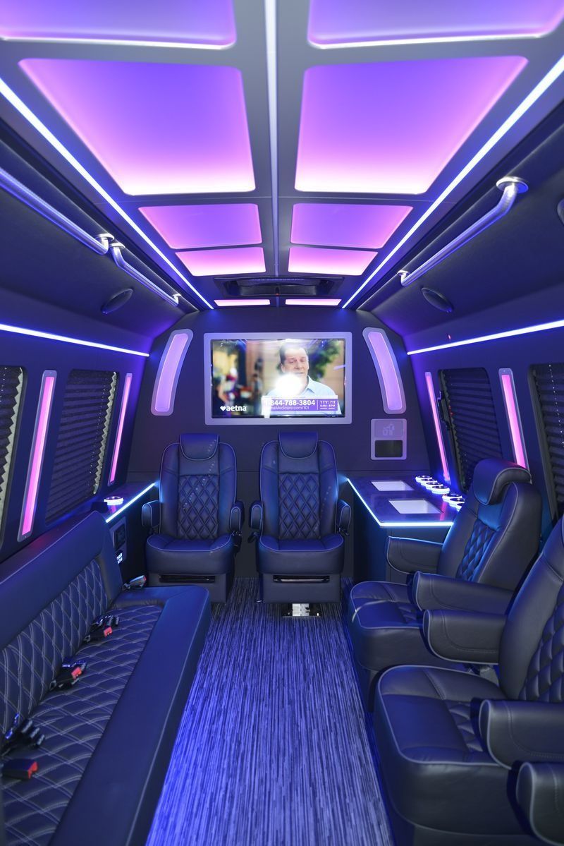 Inside of a luxury van with purple lighting, leather seats, and a TV.