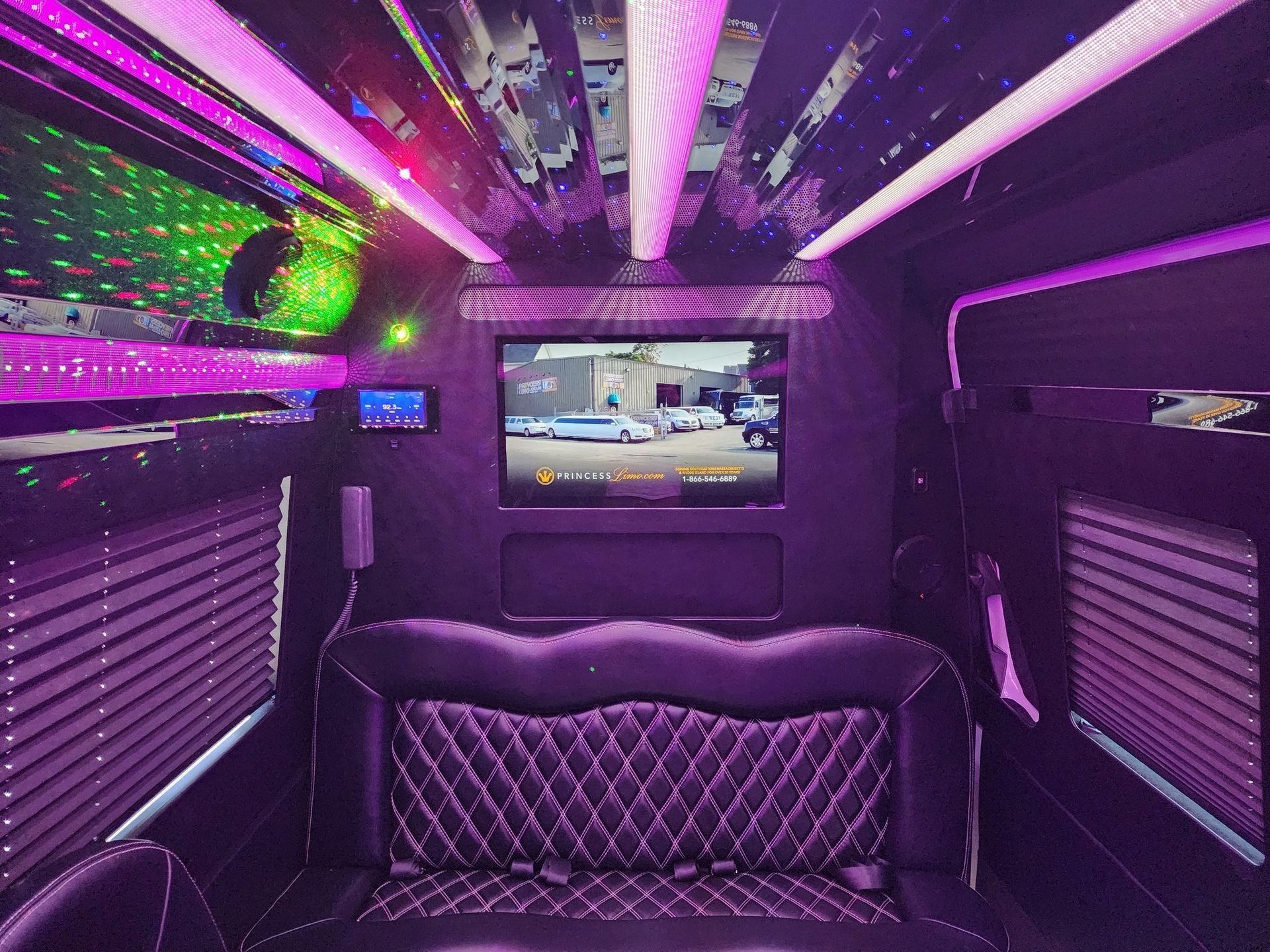 Interior of a limousine with purple lighting, a diamond-stitched seat, and a TV screen displaying a vehicle.