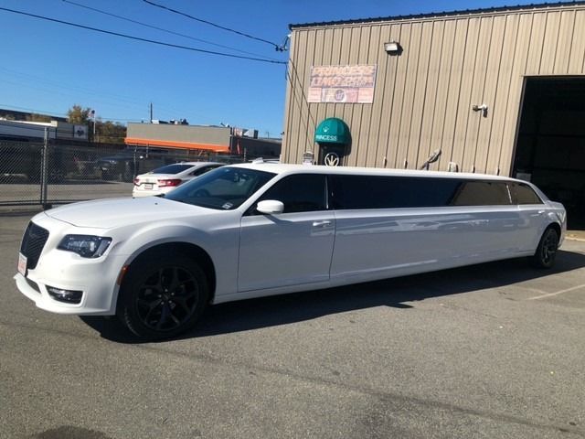 White Chrysler 300 limousine parked in front of a tan industrial building on a sunny day.