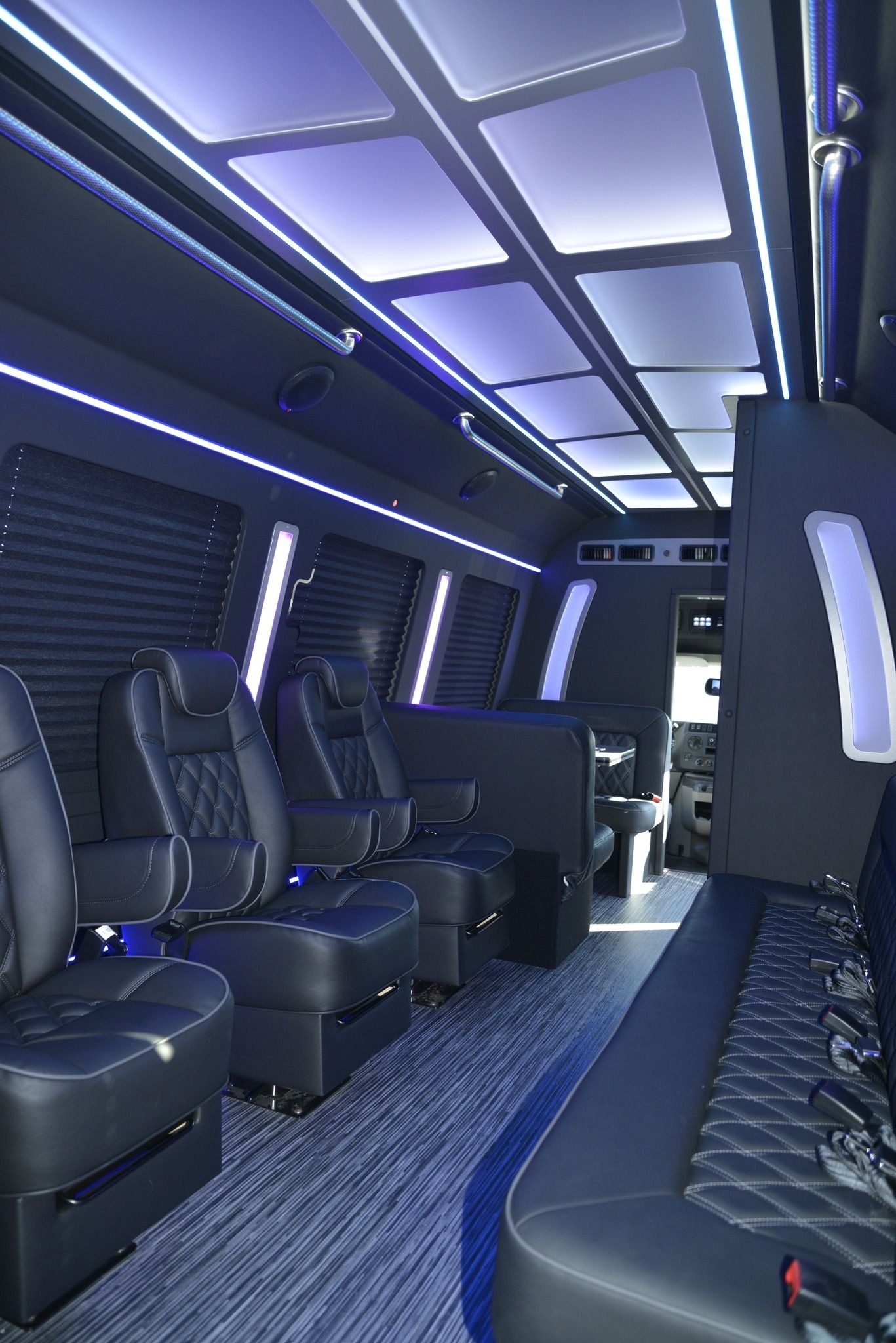 Interior of a luxury van with black leather seating, blue lighting, and wood-look flooring.