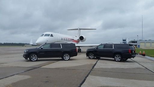 Two black SUVs parked on a runway in front of a private jet under an overcast sky.