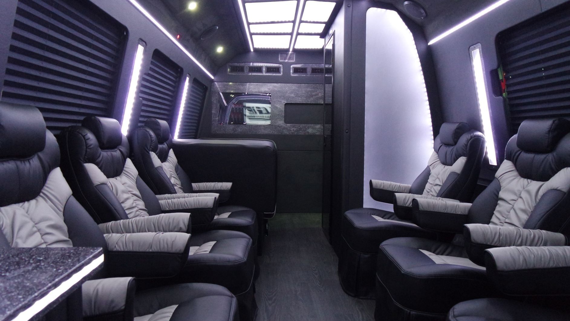 Interior of a luxury black van with leather seating, ambient lighting, and a table.