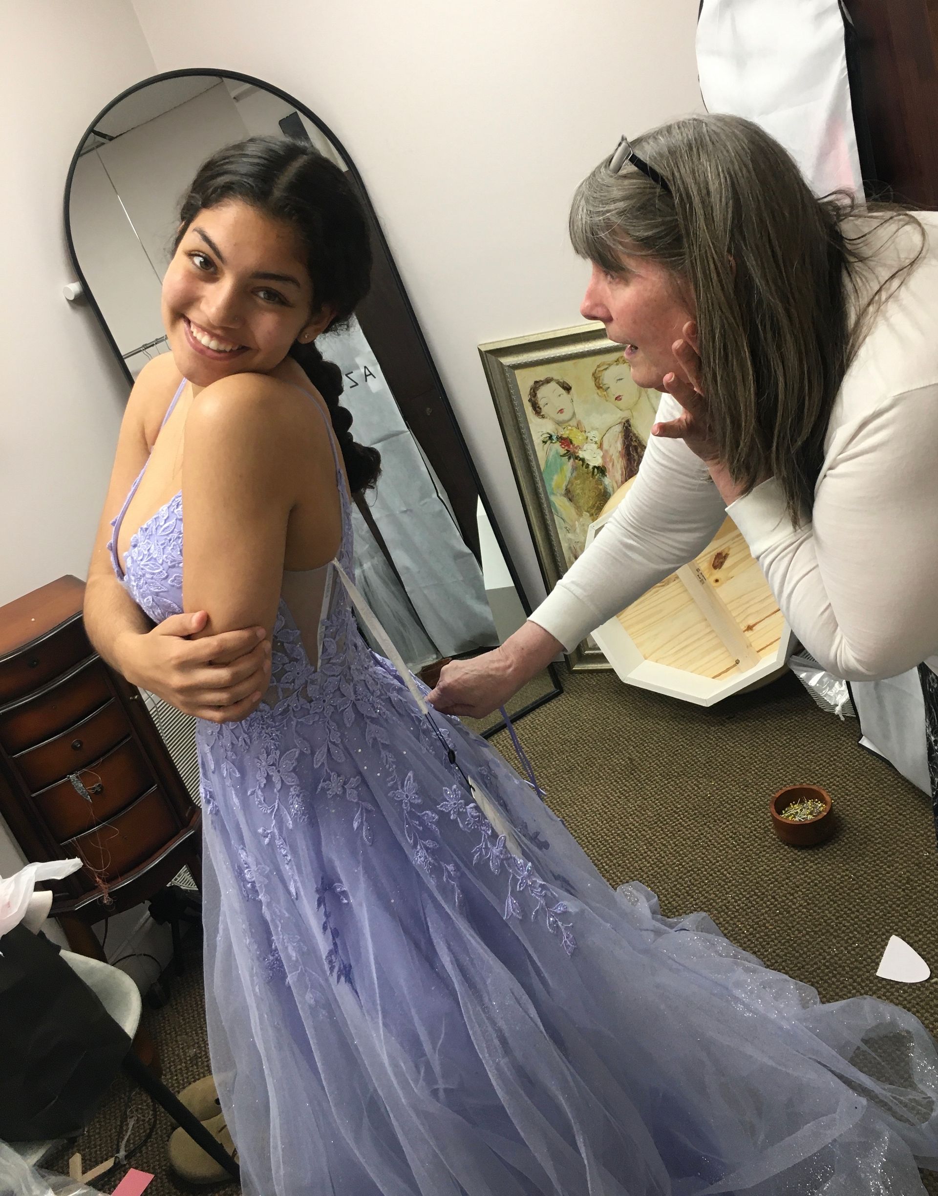 a woman is helping a woman try on a purple dress