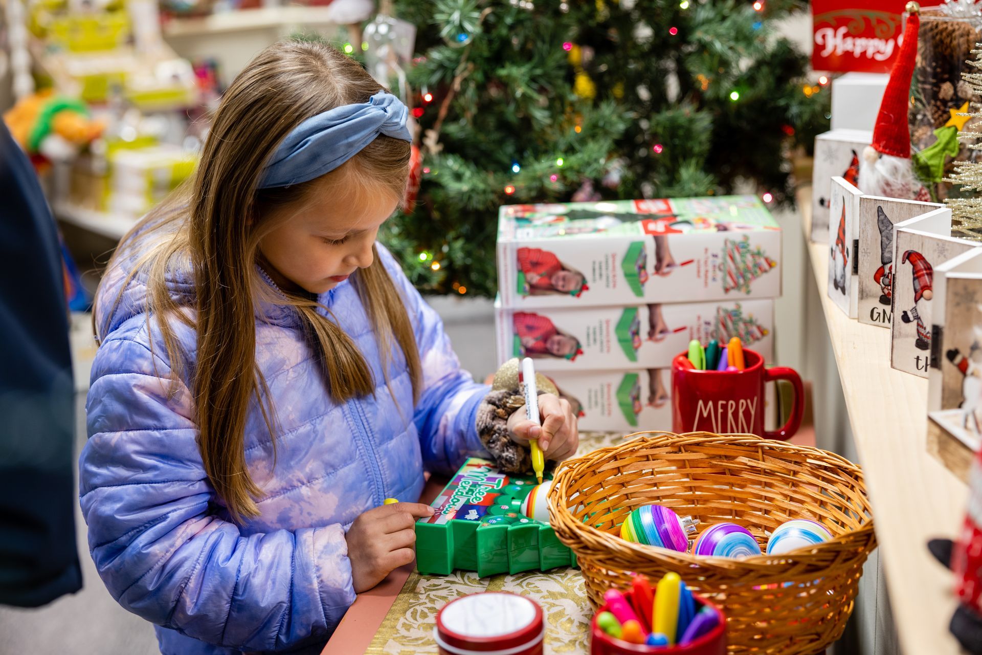 a little girl is sitting at a table decorating a Christmas tree