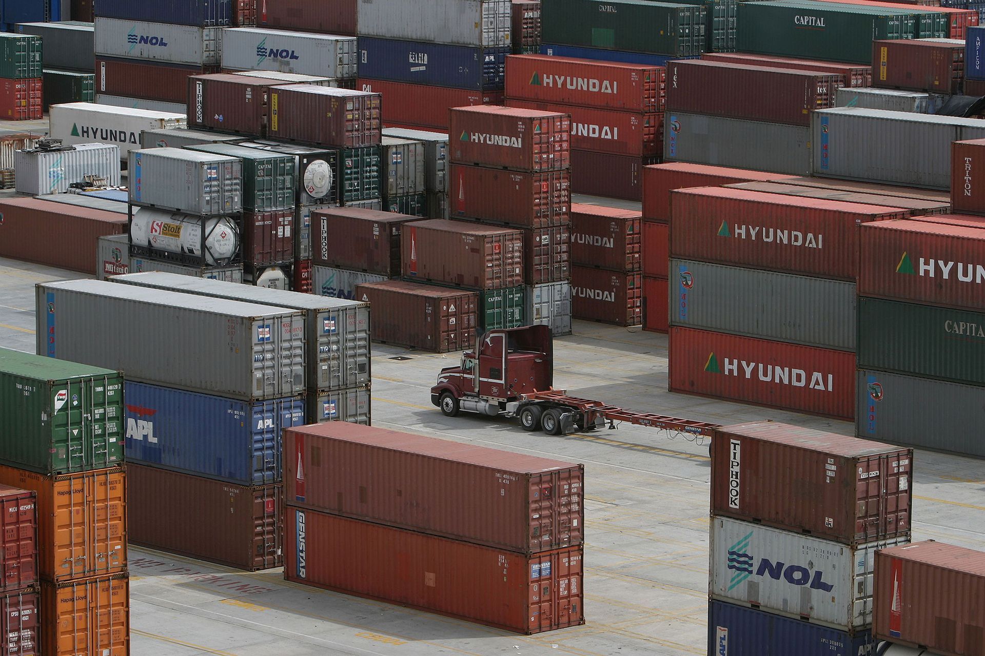 Shipping containers stacked in a port; a truck drives through the containers.