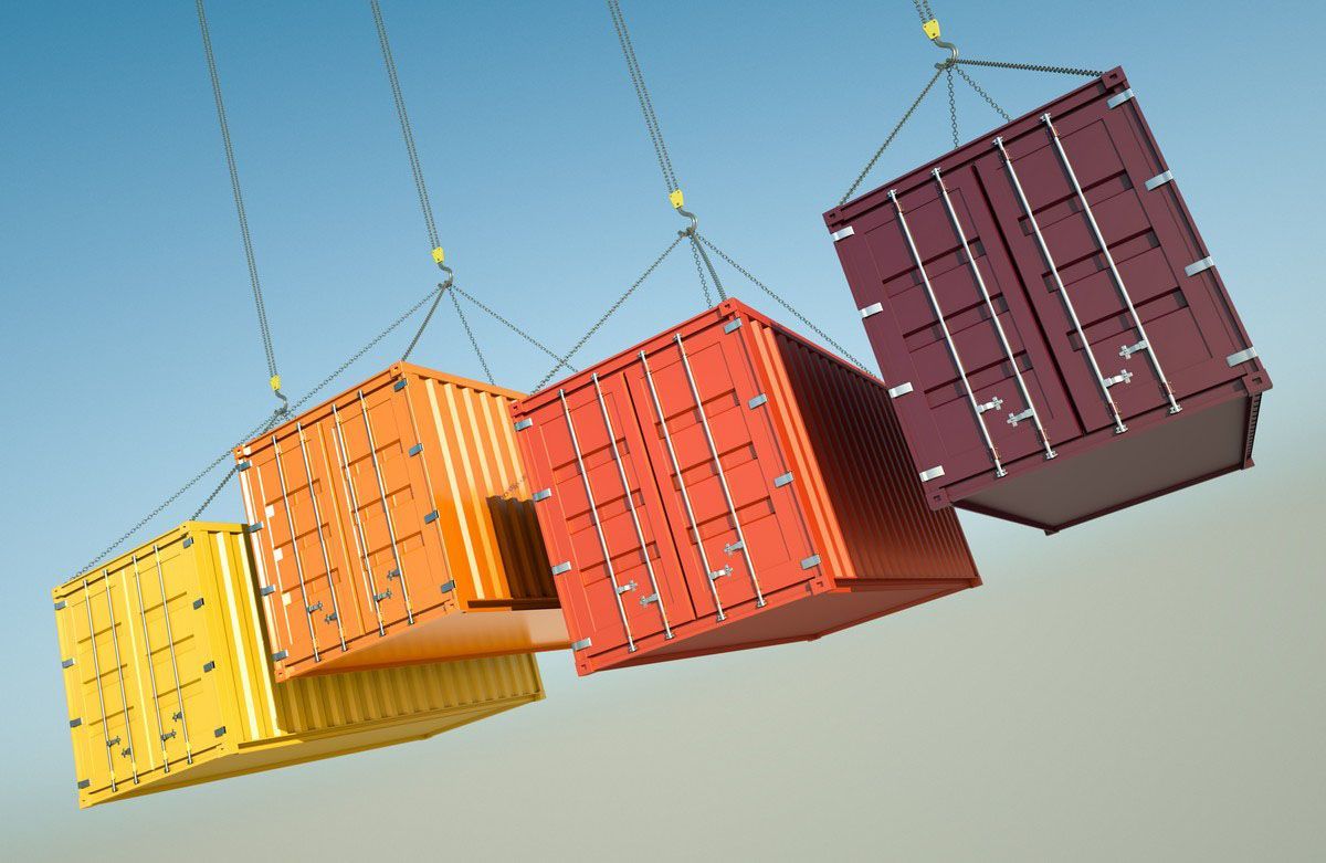 Four brightly colored shipping containers hanging from chains against a blue sky.