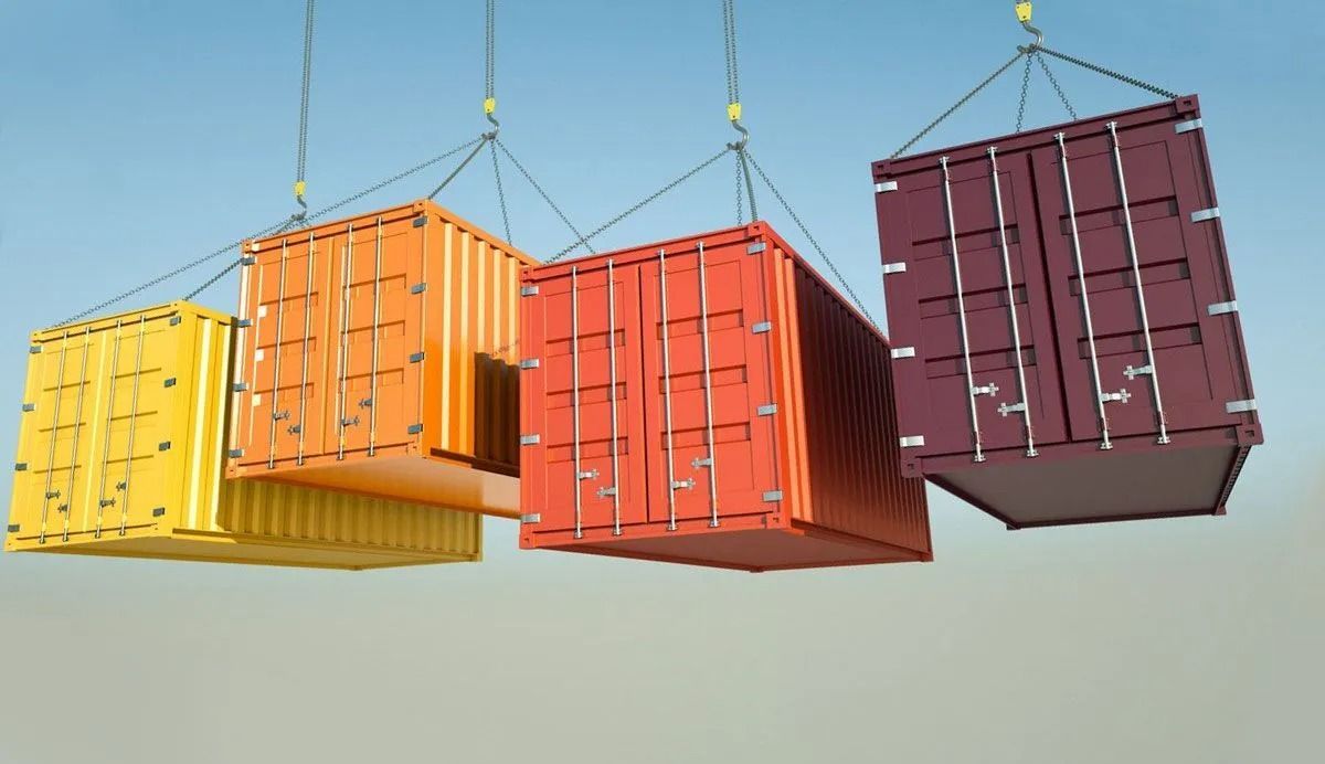 Four colorful shipping containers suspended in the air by crane cables.