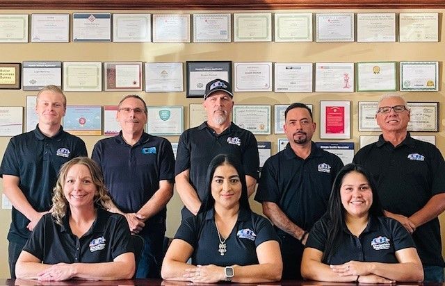 Group of people in black shirts posing in front of framed certificates.