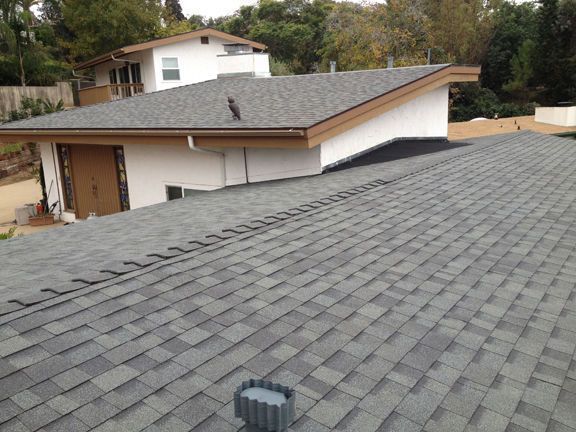 Gray shingled roof of a house with white walls, brown trim, and a vent stack.