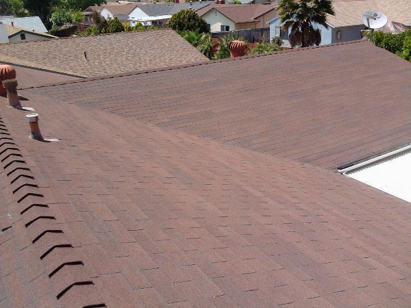 Brown asphalt shingle roof on a house, with several other homes in the background. Sunny day.
