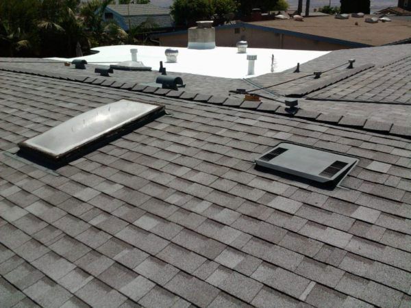 Asphalt shingle roof with two skylights and roof vents, sunny day.