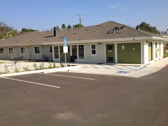 A single-story light green building with a gray roof and accessible parking.