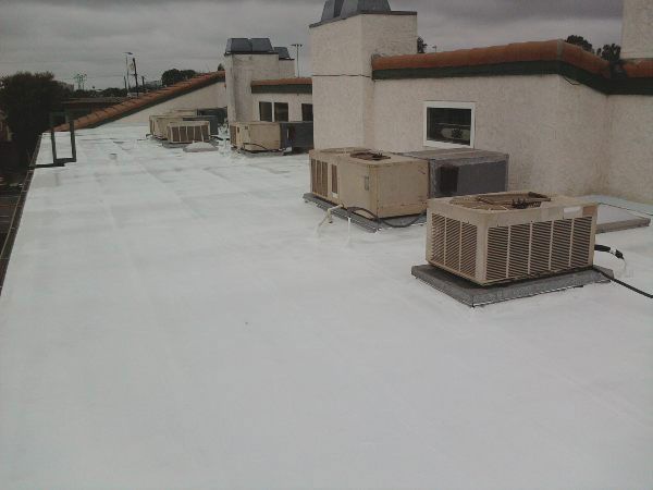 White flat roof with AC units on top of a building with a cloudy sky.