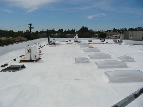 Flat, white commercial roof with skylights and equipment, under a blue sky.