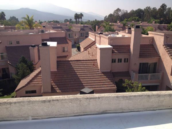 Pink stucco townhouses with terra cotta tile roofs, chimneys, and trees, with mountains in the background.