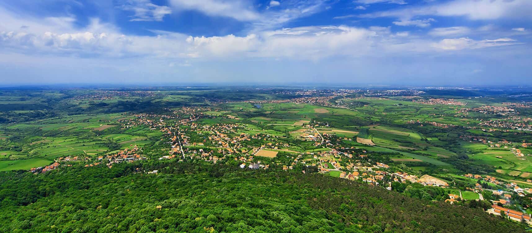 Aerial view of a green landscape with buildings and a cloudy blue sky.