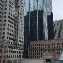 Urban cityscape featuring a modern glass skyscraper reflecting neighboring buildings amidst surrounding stone structures.