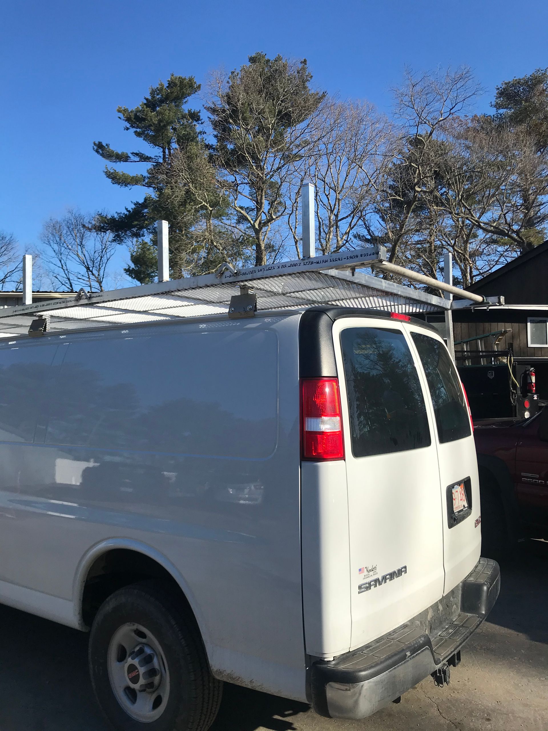 A white work van parked outdoors, featuring a metal roof rack with upright supports against a clear blue sky.