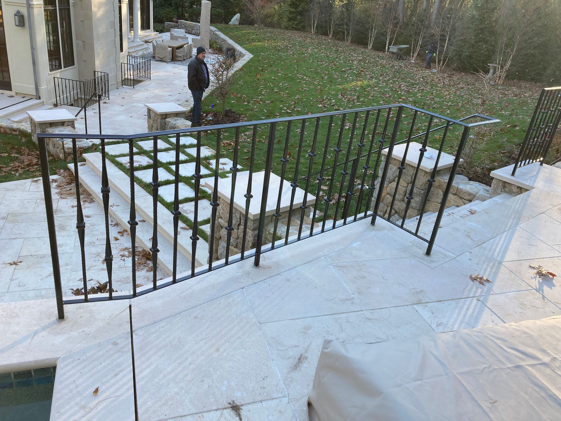A black wrought iron railing borders a stone patio and steps overlooking a backyard lawn.