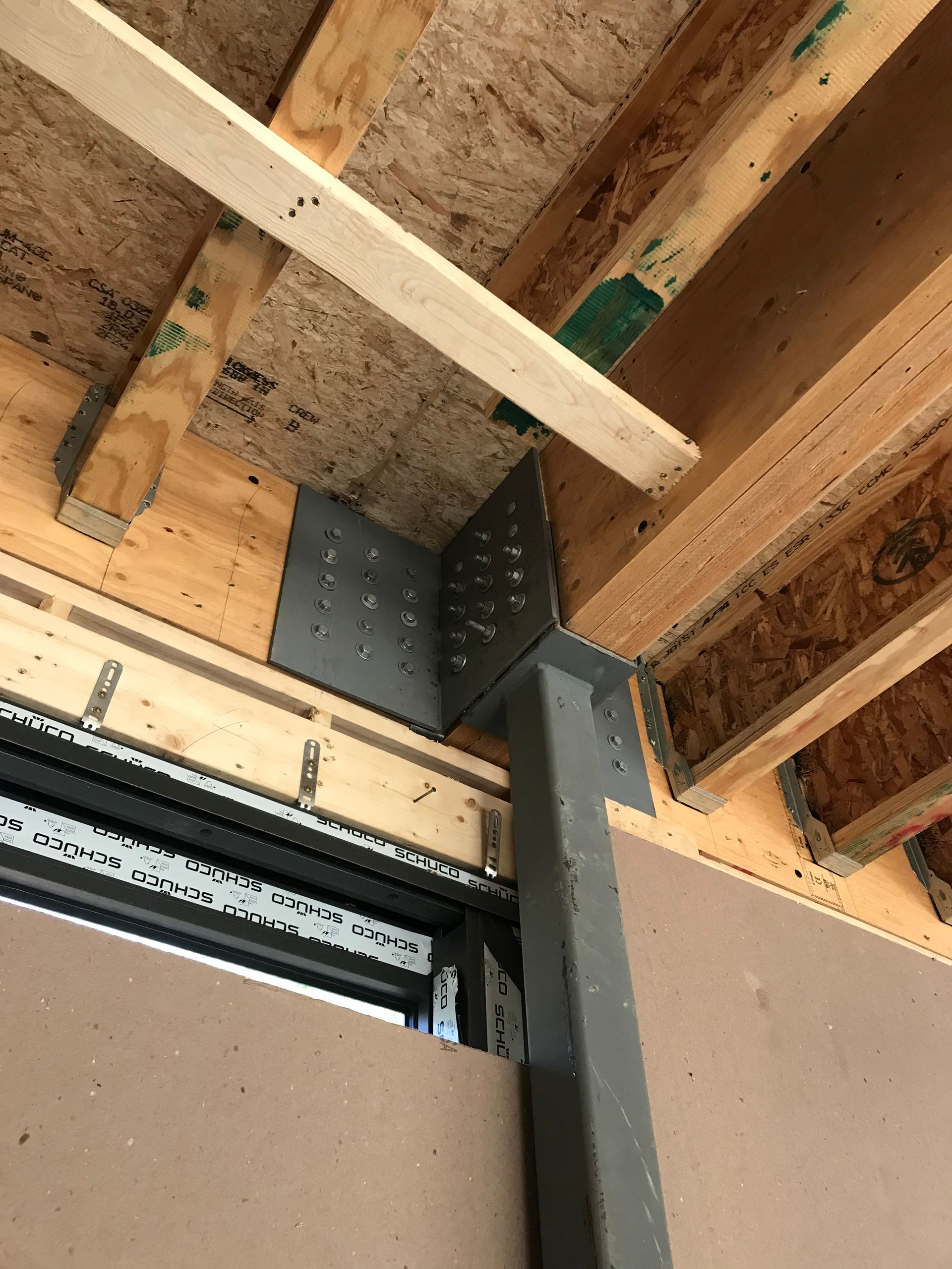 A steel post and bracket assembly supporting wooden floor joists and ceiling beams in a residential construction frame.