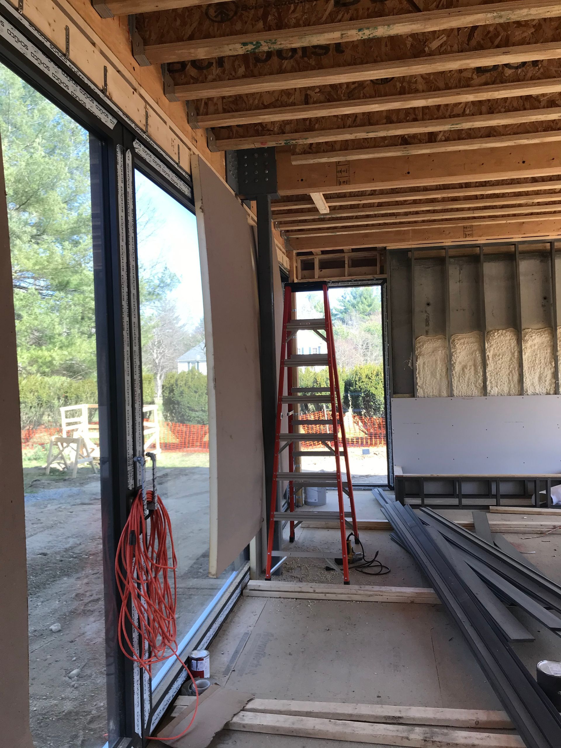 Interior construction site with an exposed ceiling, a red ladder, framing, and a large sliding door opening.