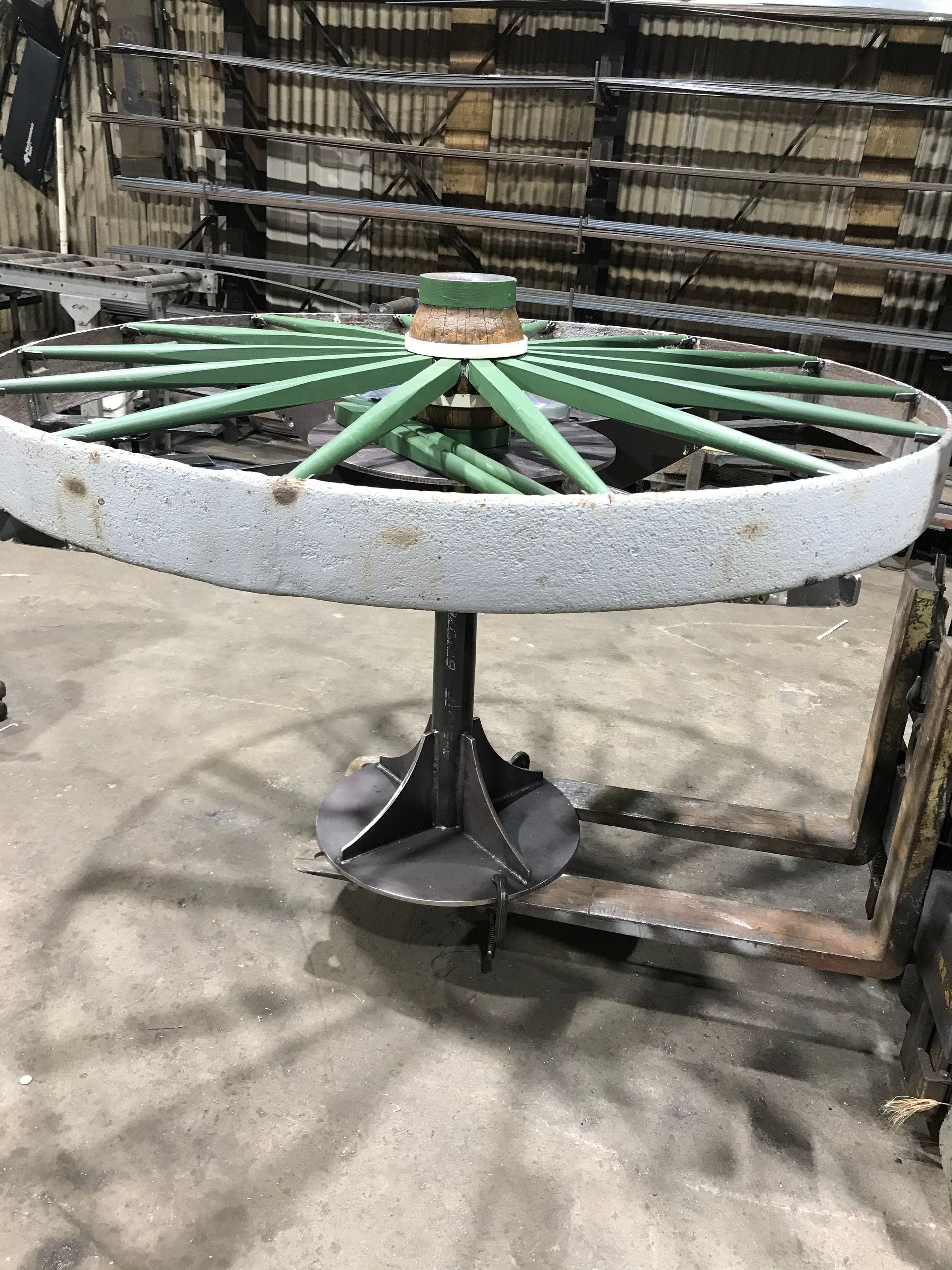 A large green wagon wheel with a textured, wide rim resting on a metal stand inside a workshop.