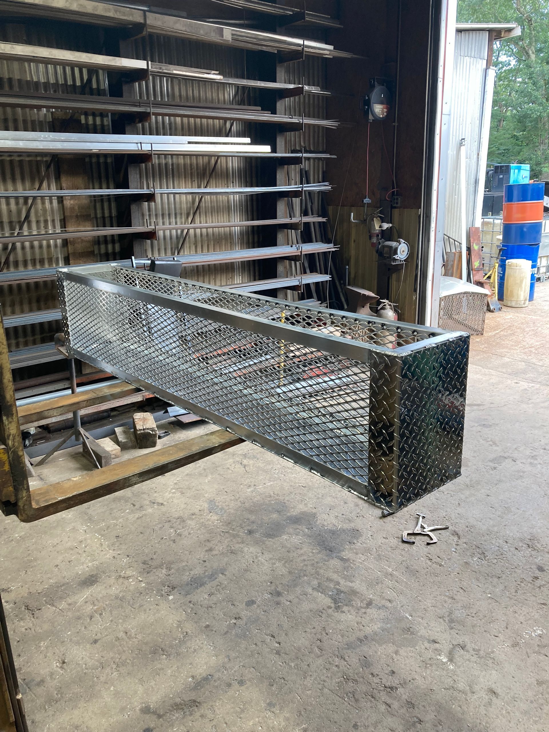 A long, rectangular metal box with a perforated diamond-plate pattern hangs in a workshop setting.