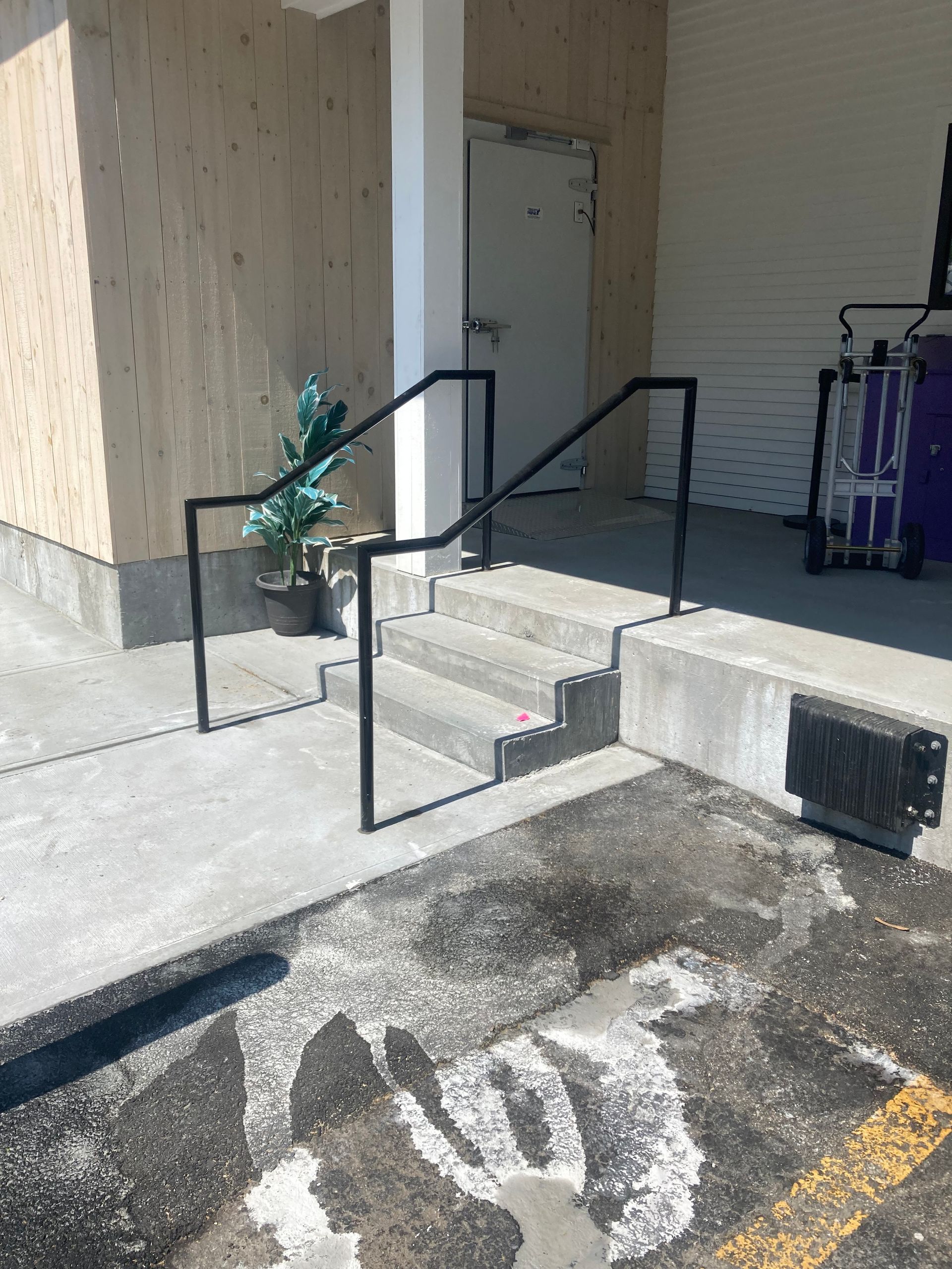 A black metal handrail flanking concrete stairs leading to a white door in a loading dock area.