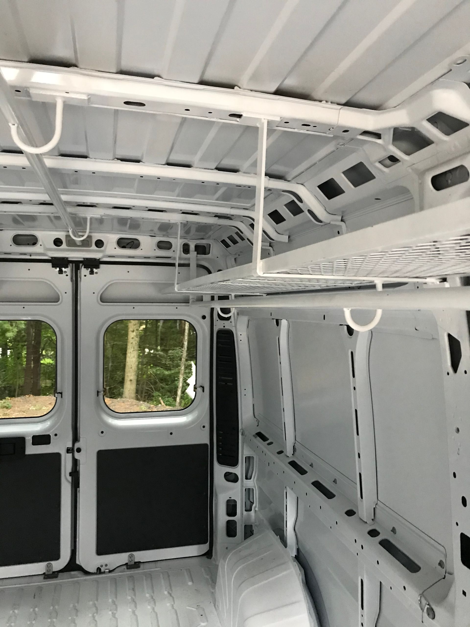 The interior of an empty white van showing a metal storage rack mounted to the ceiling and sidewall.