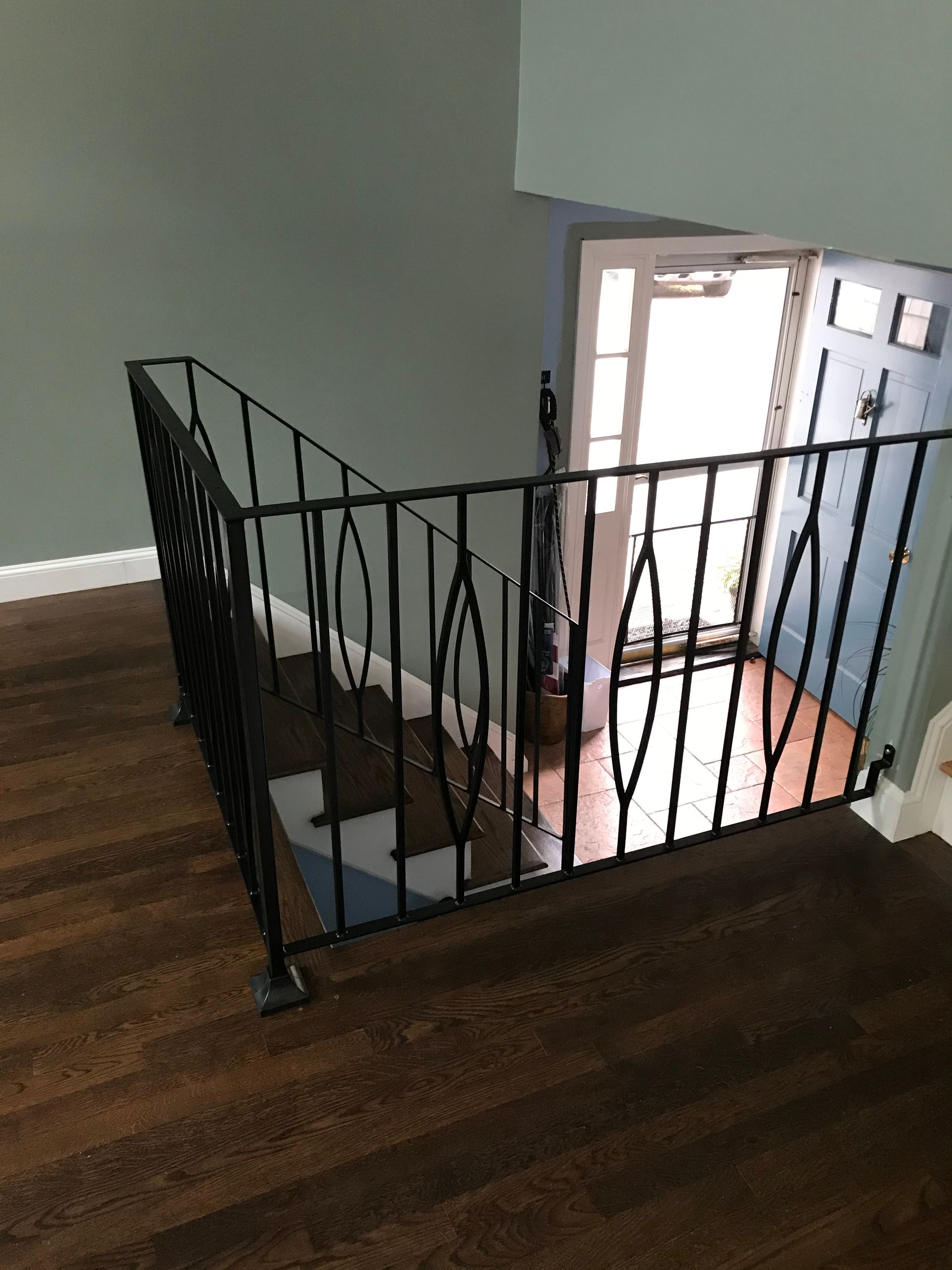 Black iron railing with diamond accents surrounding a stairwell overlooking an entryway with a light blue door.