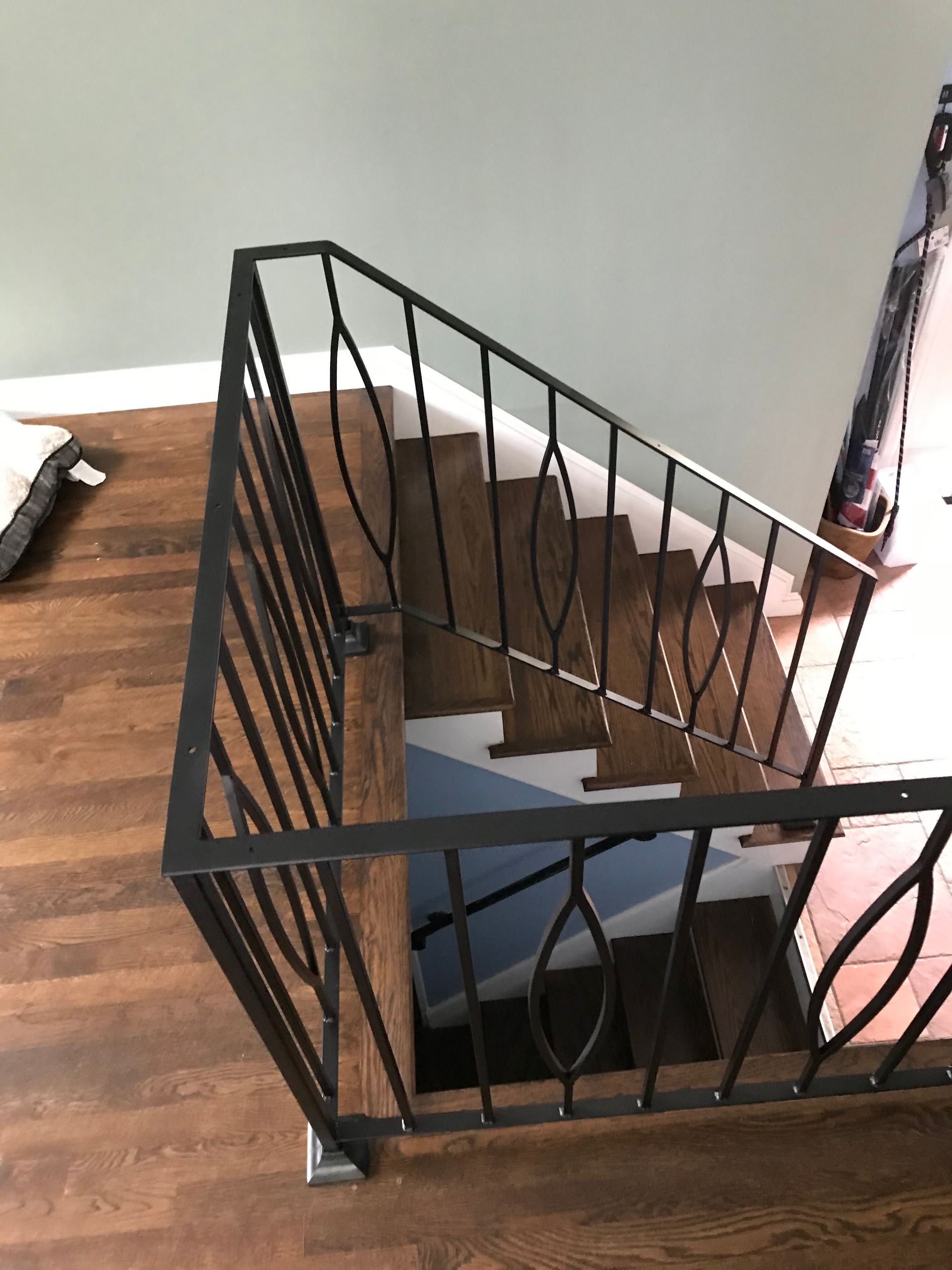 A view from above of wooden stairs with a black metal railing featuring decorative diamond-shaped patterns.
