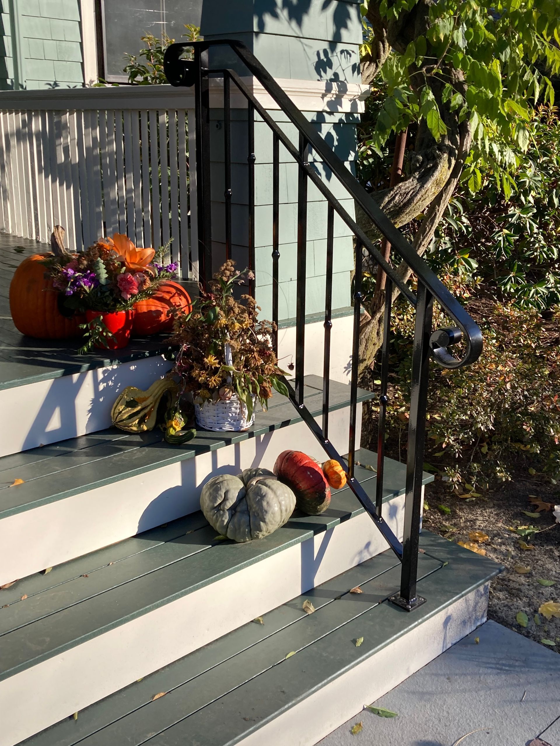 Autumnal decor including pumpkins, gourds, and flowers arranged on teal porch steps next to a black metal handrail.