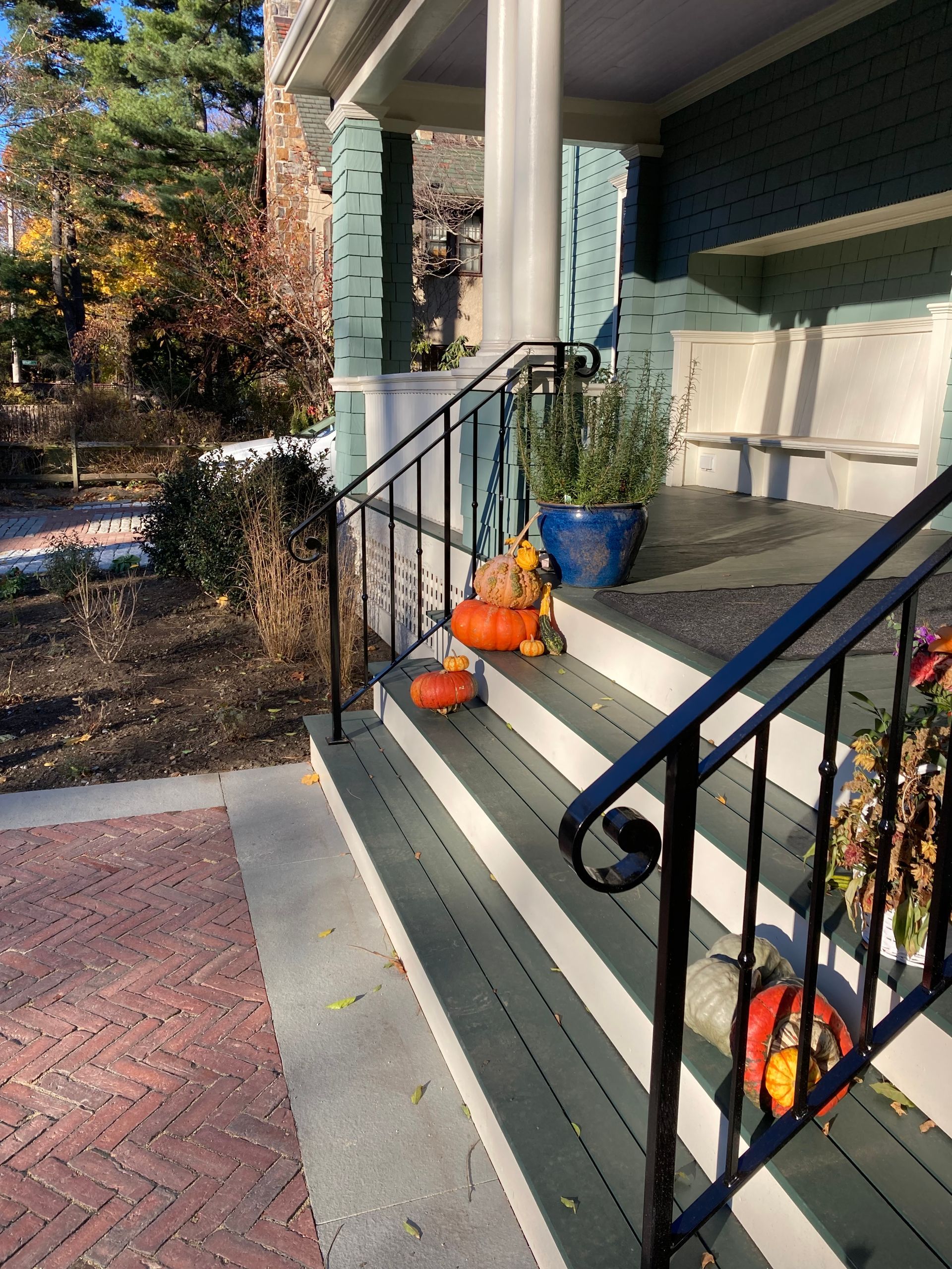 Green porch steps decorated with pumpkins and a potted plant, leading to a home entrance with a brick walkway nearby.