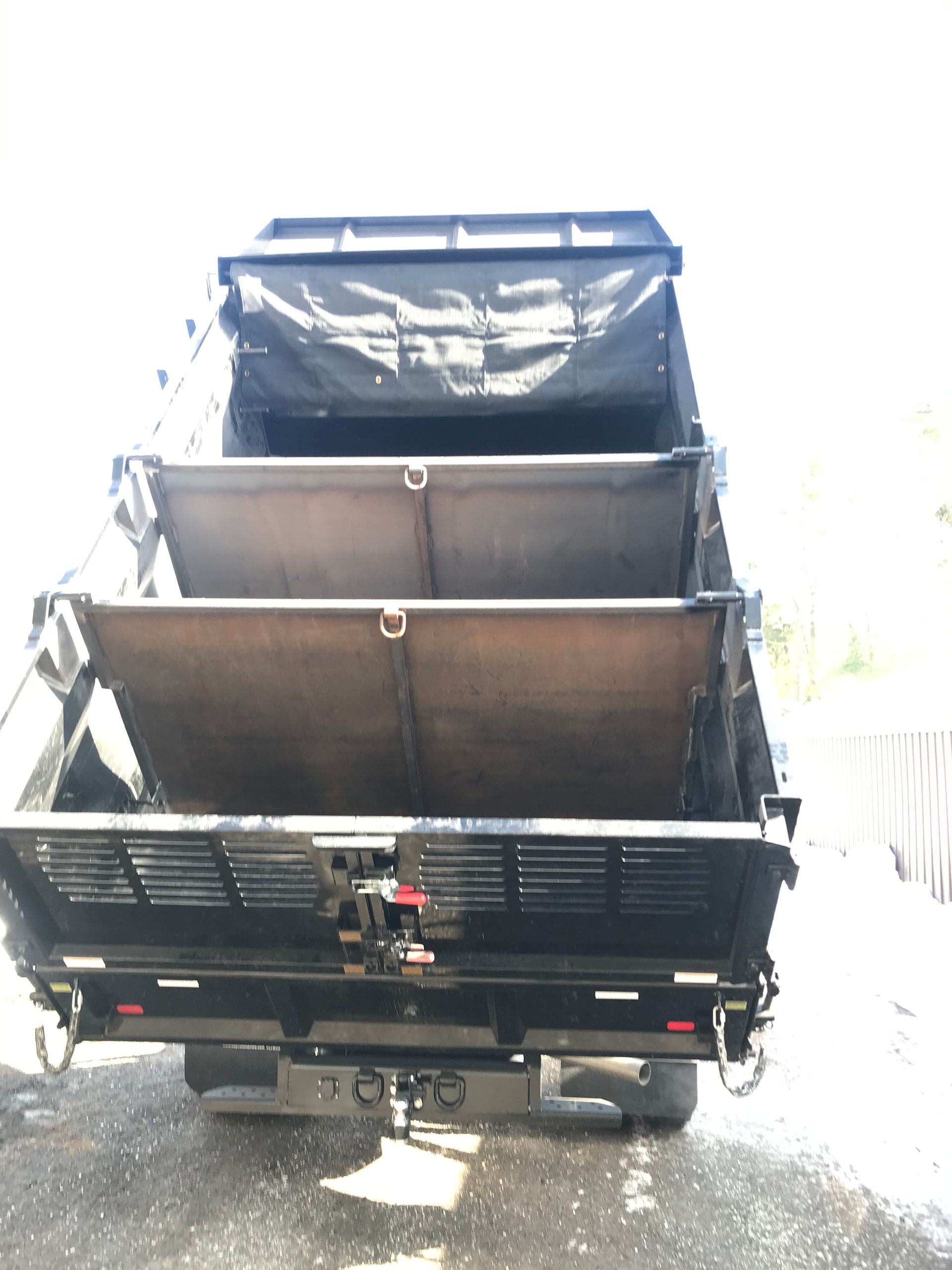 A black trailer with multiple hinged, stacked metal panels opened outward, revealing its interior structure.