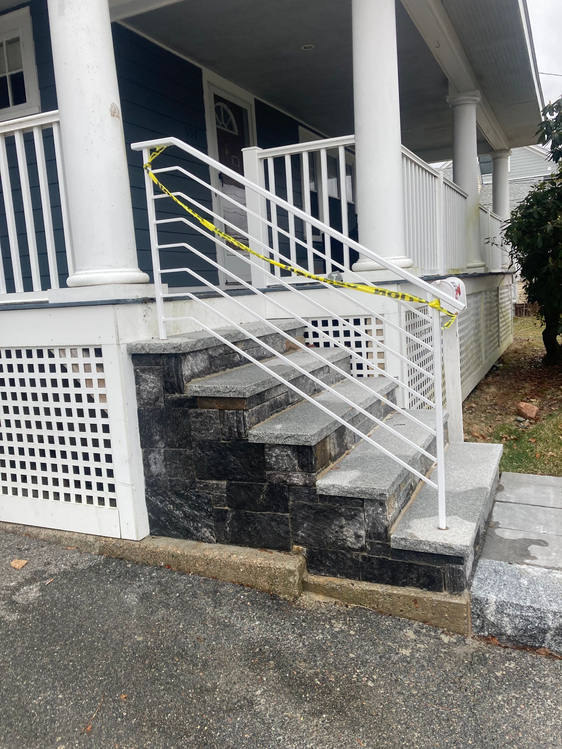 A stone staircase leading to a porch is blocked by a white metal handrail wrapped in yellow caution tape.
