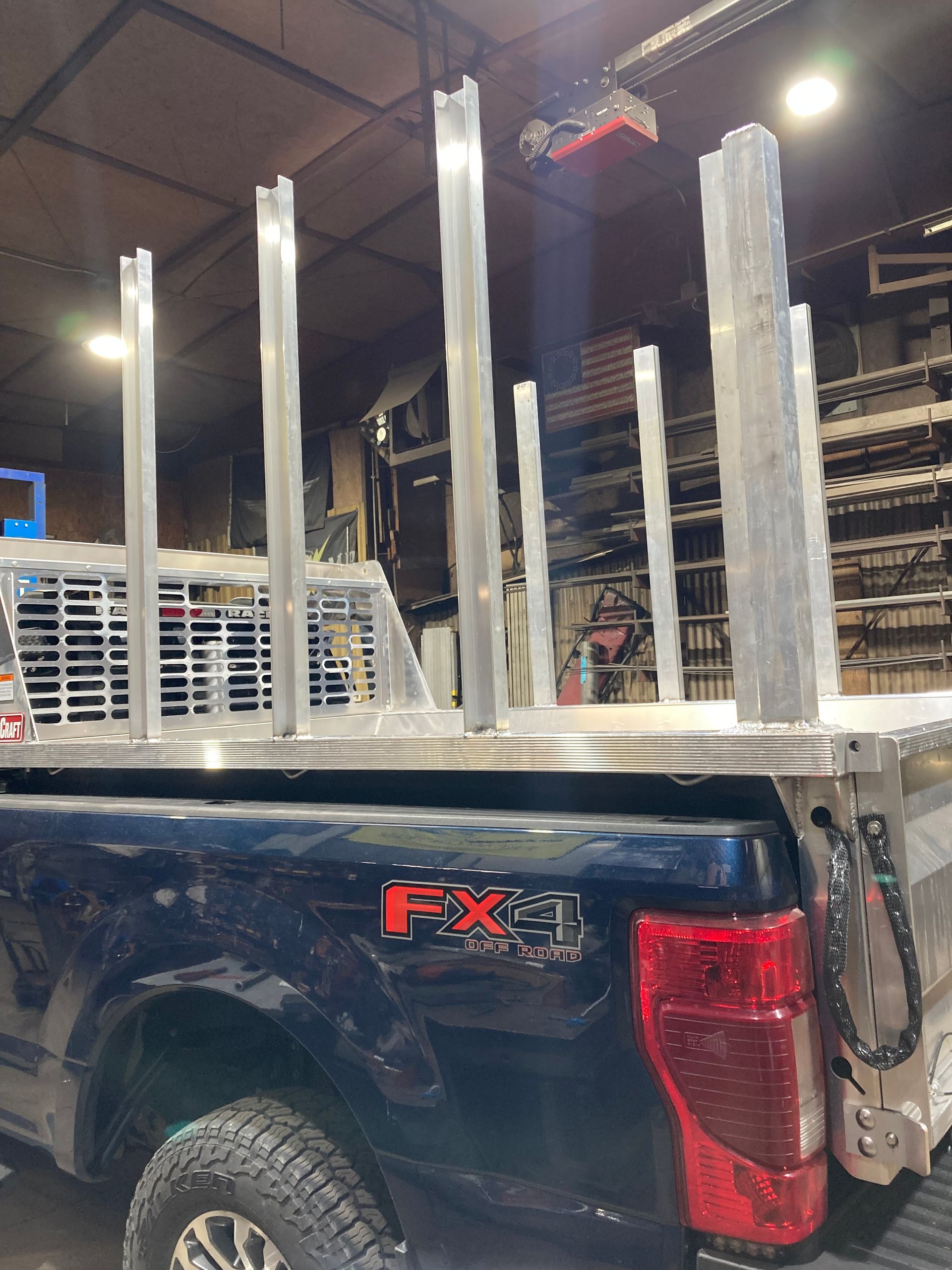 A dark pickup truck with an FX4 decal features several vertical metal racks installed in the bed inside a workshop.