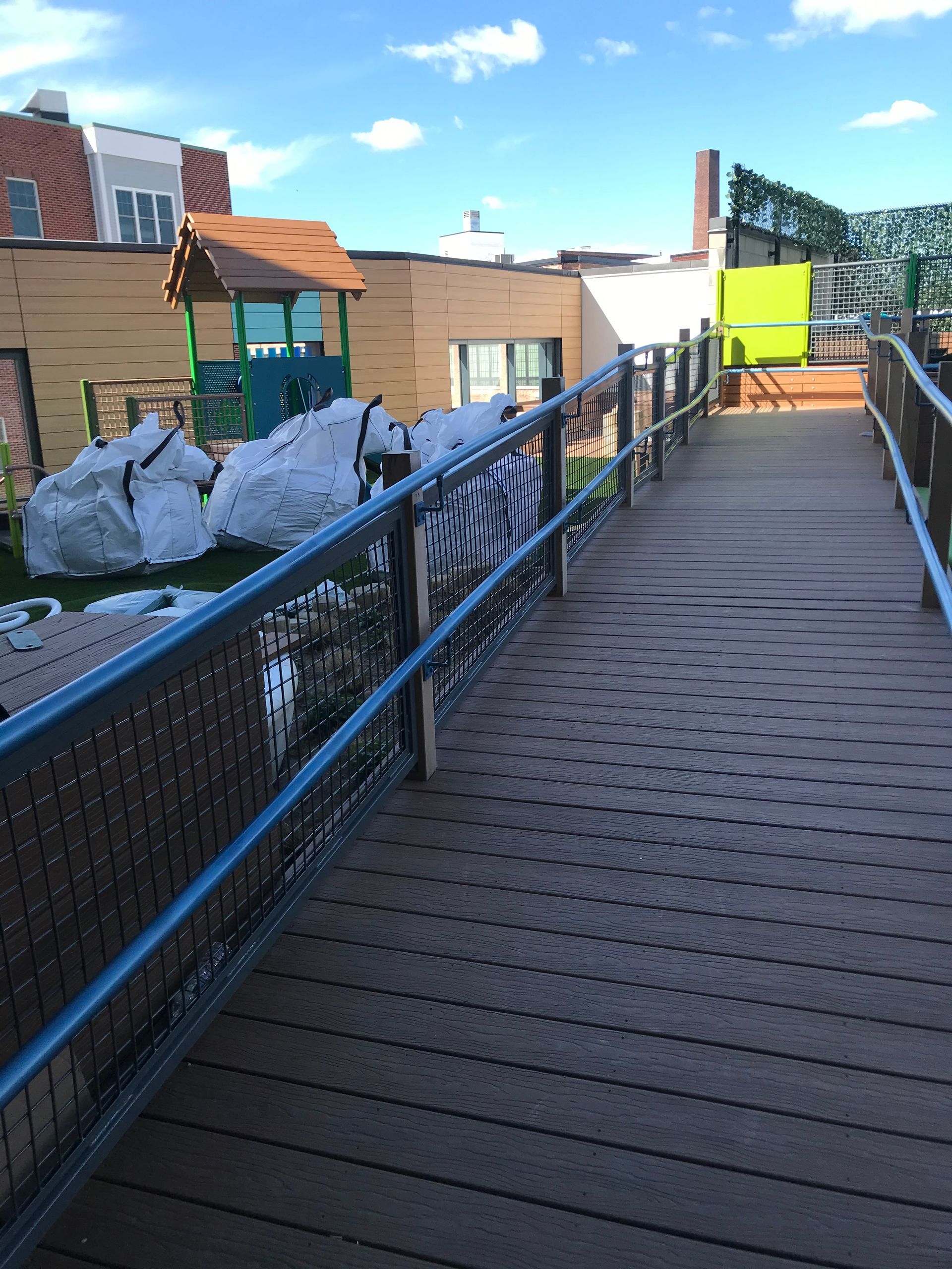 A wooden walkway leads to a playground with white, rock-like climbing structures under a blue sky.