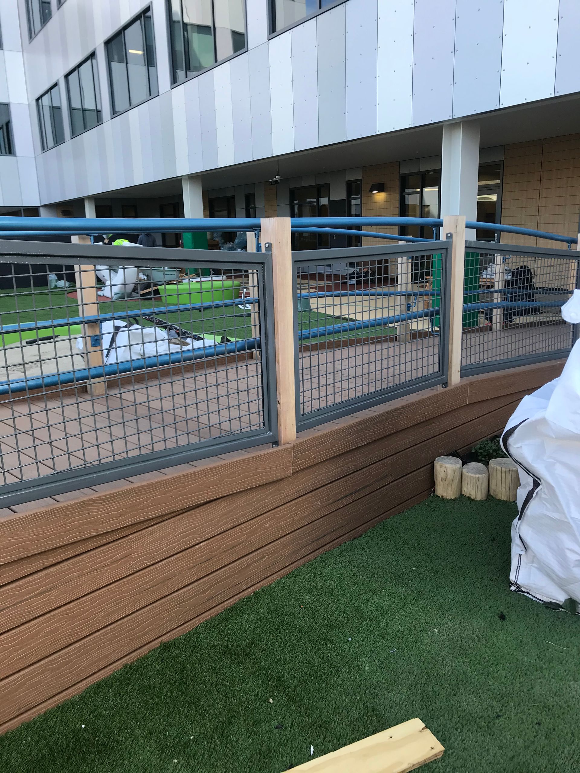 A view of a tan multi-tiered retaining wall with a metal railing along a walkway in front of a modern building.