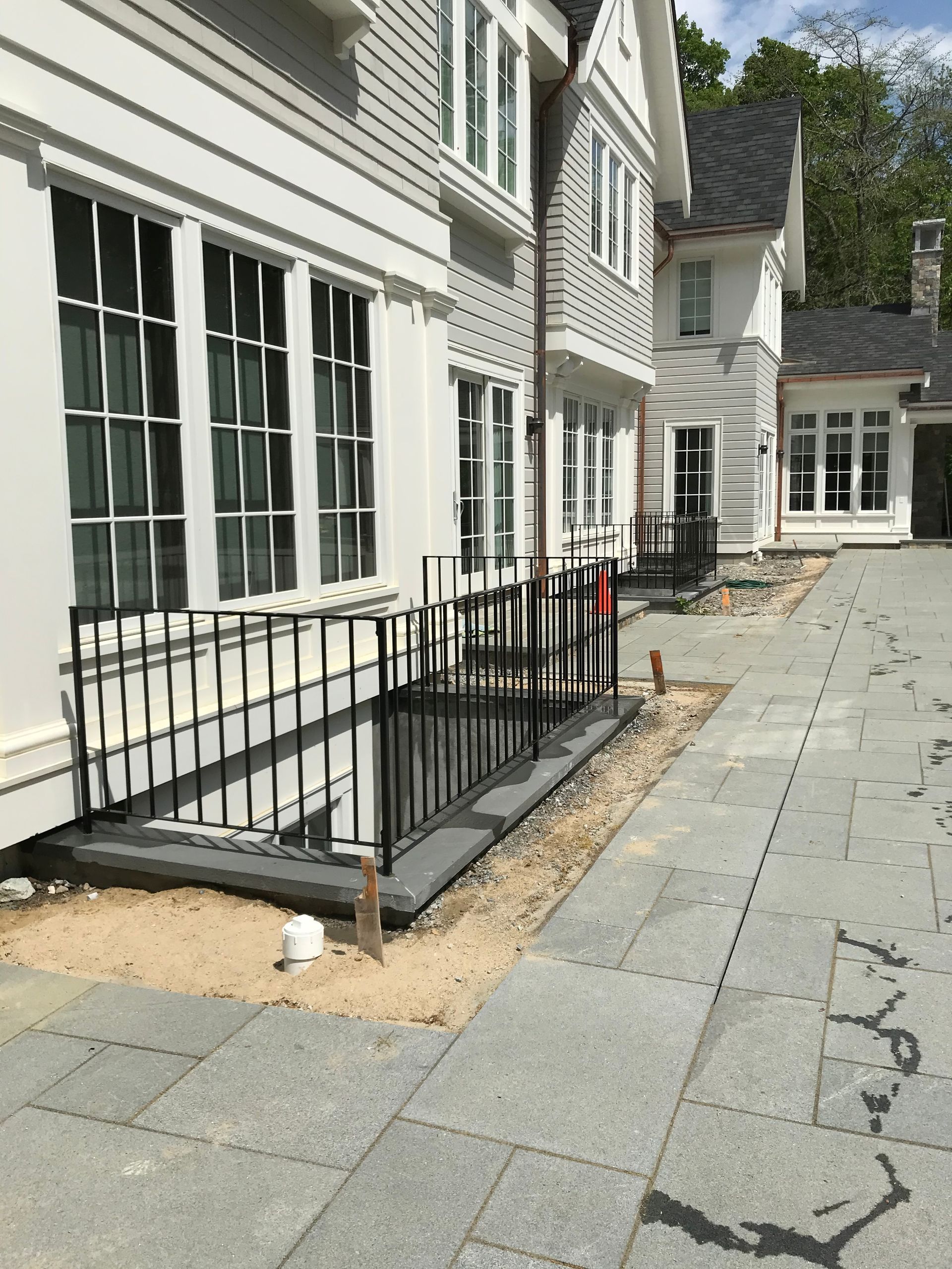 An exterior view of a white multi-story house with a black metal railing around a sunken basement window well.