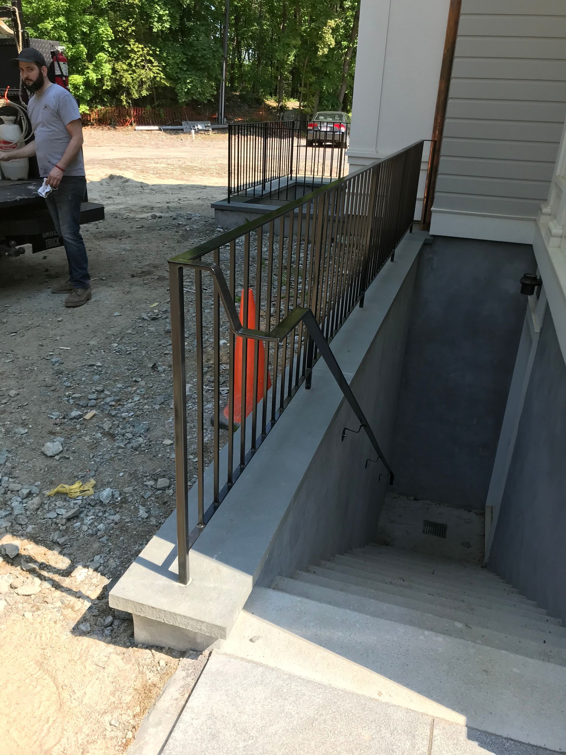 Concrete basement stairs with a decorative metal railing next to a building under construction.