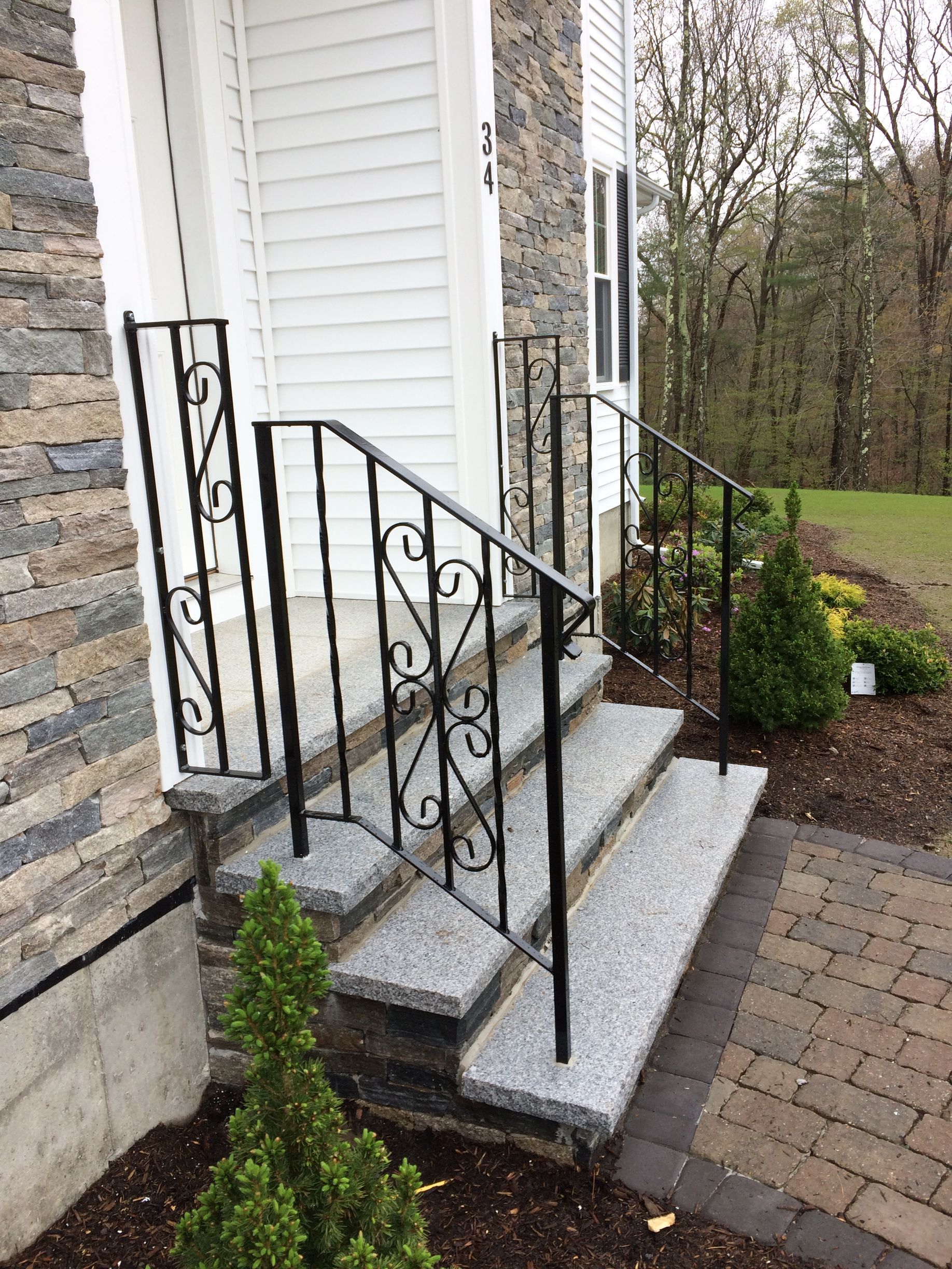 Granite steps with black metal wrought iron railings leading to a white door at a building entrance.
