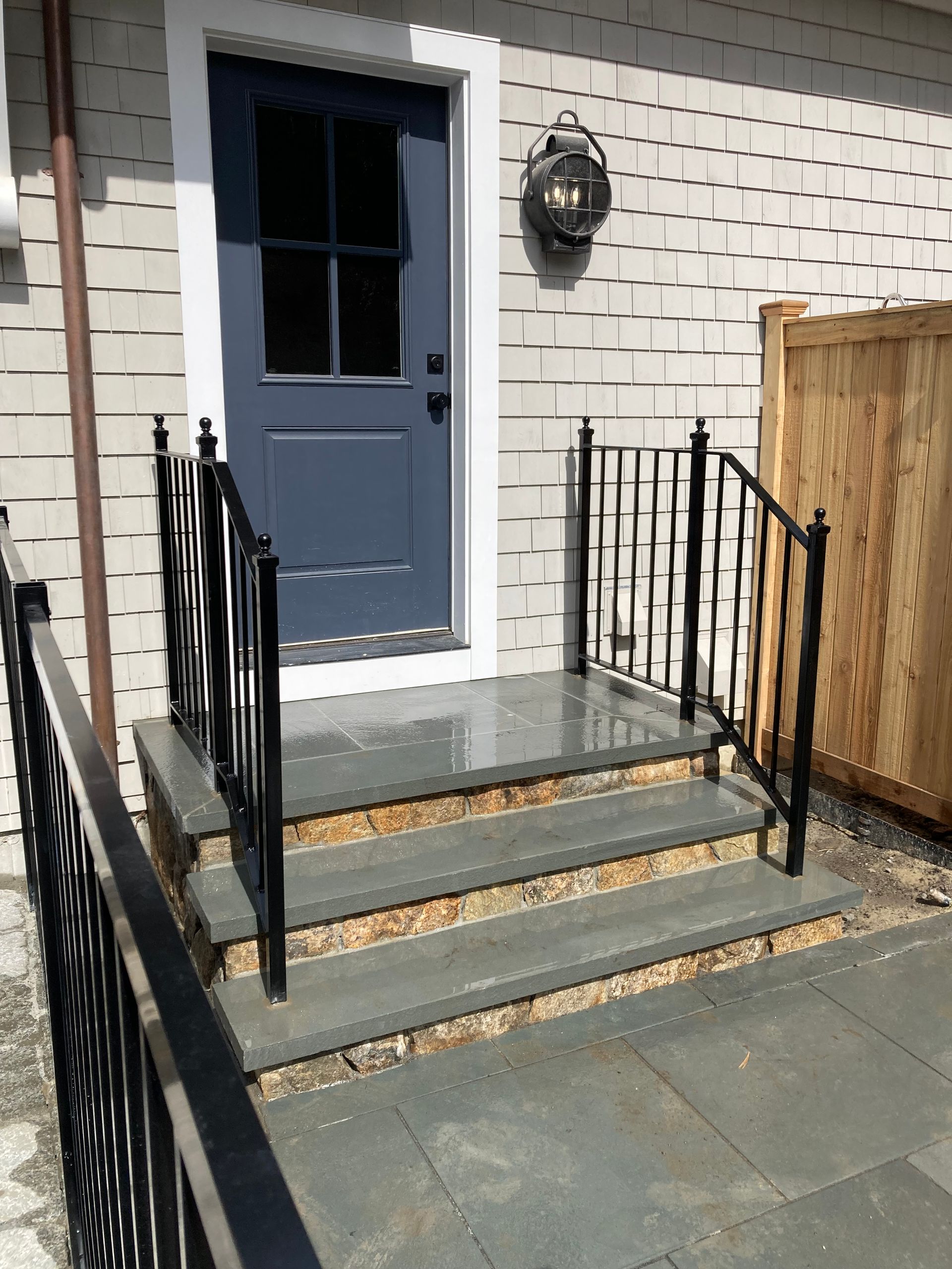 A blue door with a black lantern fixture, accessed by three stone steps featuring black iron railings on both sides.