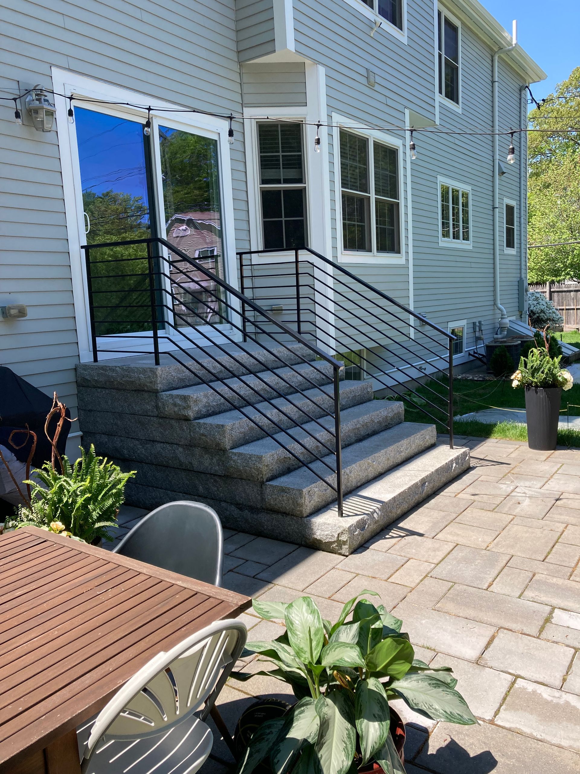 Gray stone steps with black metal railings leading to a sliding glass door on a house with light gray siding and a patio.